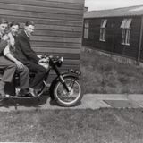 M184 Three RAF men in civvies on a Norton motorbike among the huts at 