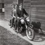 M185 Three RAF men in civvies on a Norton motorbike among the huts at 